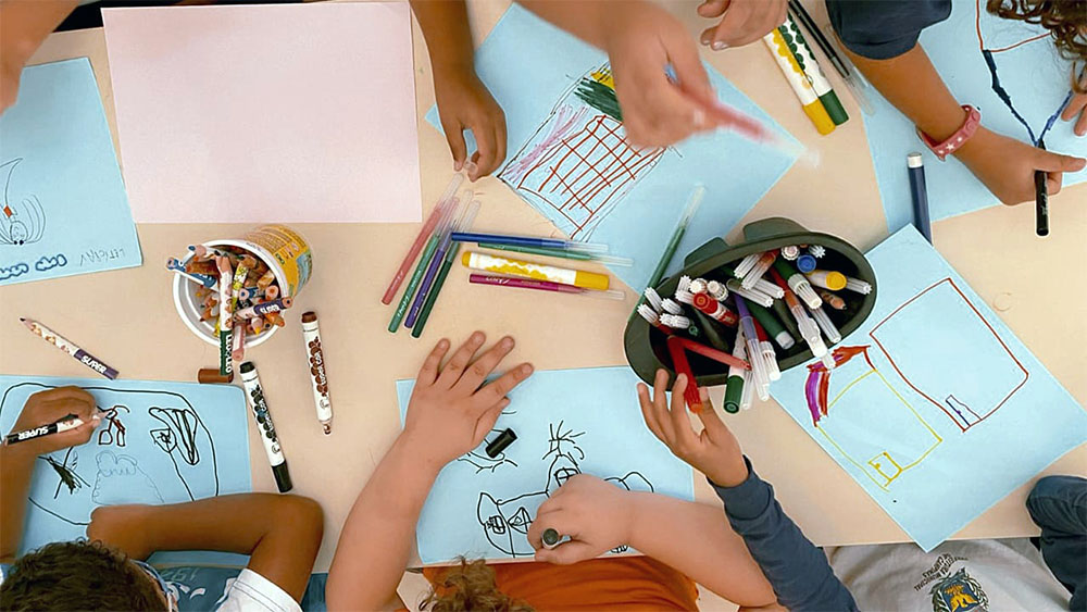 Várias crianças desenhando em uma mesa de escola